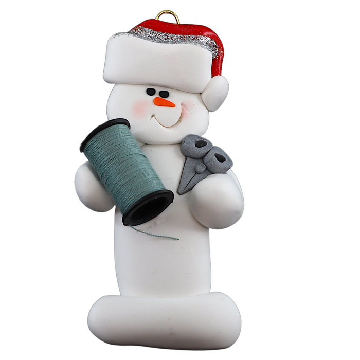Ornament of white snowman in red hat holding a spool of thread and scissors.