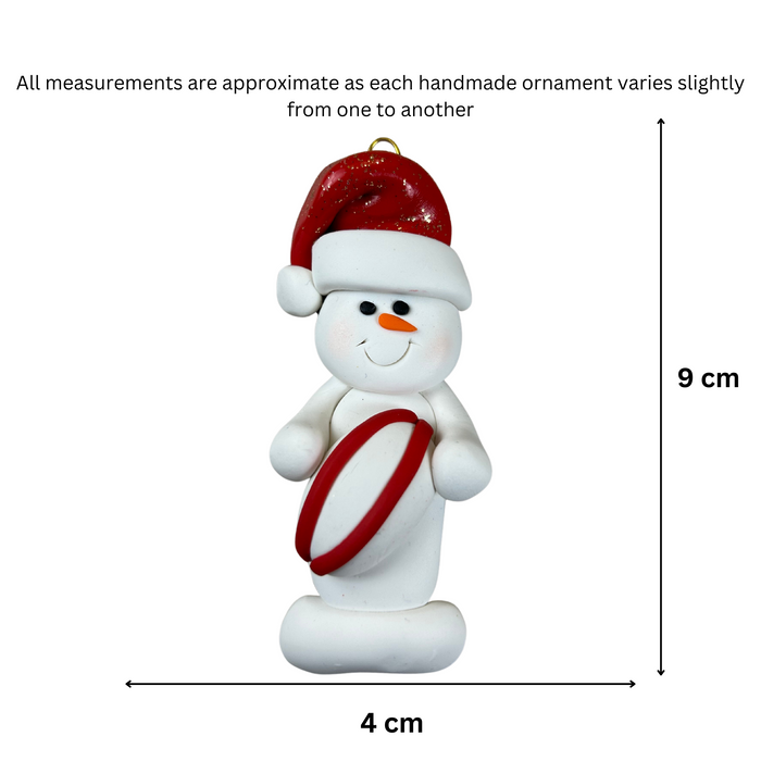 Ornament of white snowman in red hat holding a red and white rugby ball, graphed to show size (4x9cm).