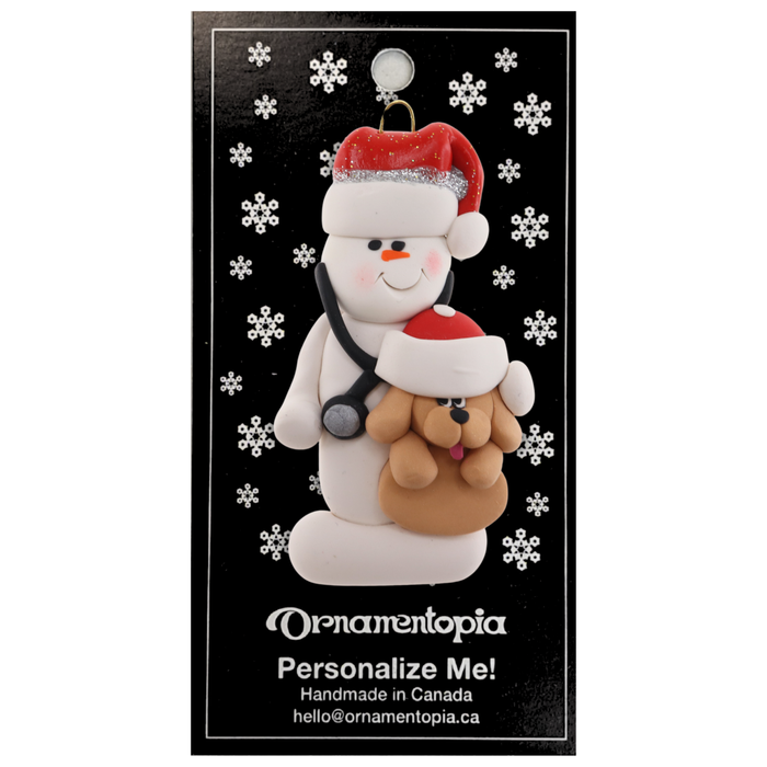 Ornament of white snowman in red hat holding a tan dog and stethoscope, on display backing card.