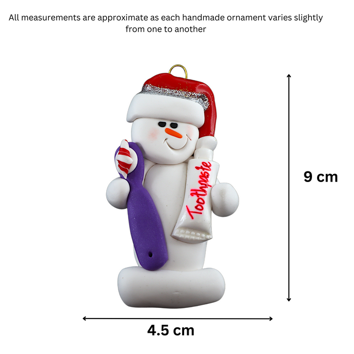 Ornament of white snowman in red hat holding a toothbrush and toothpaste, graphed to show size (4.5x9cm).