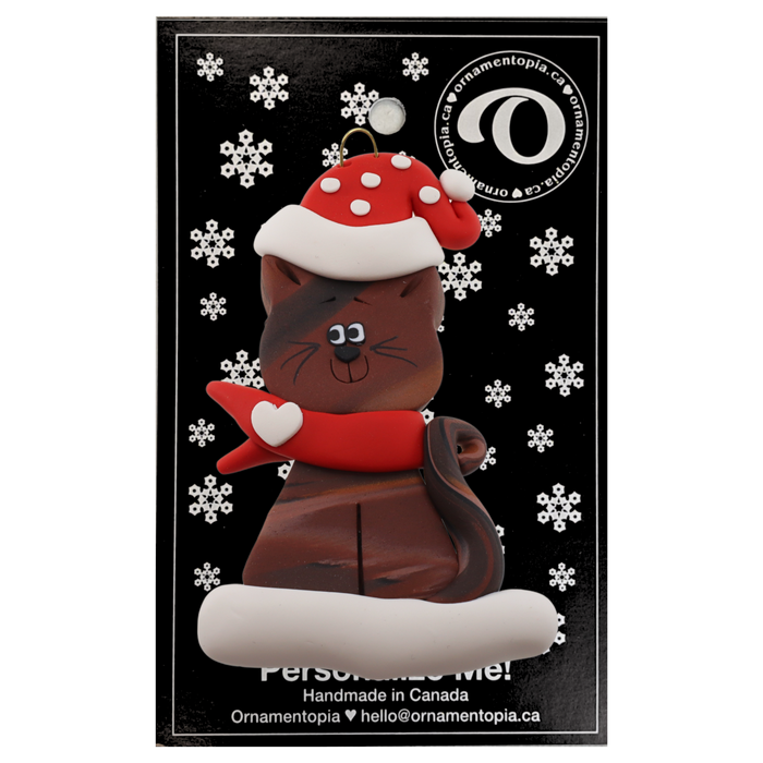 Ornament of brown cat in red and white polka dot Christmas hat and scarf, on display backing card.