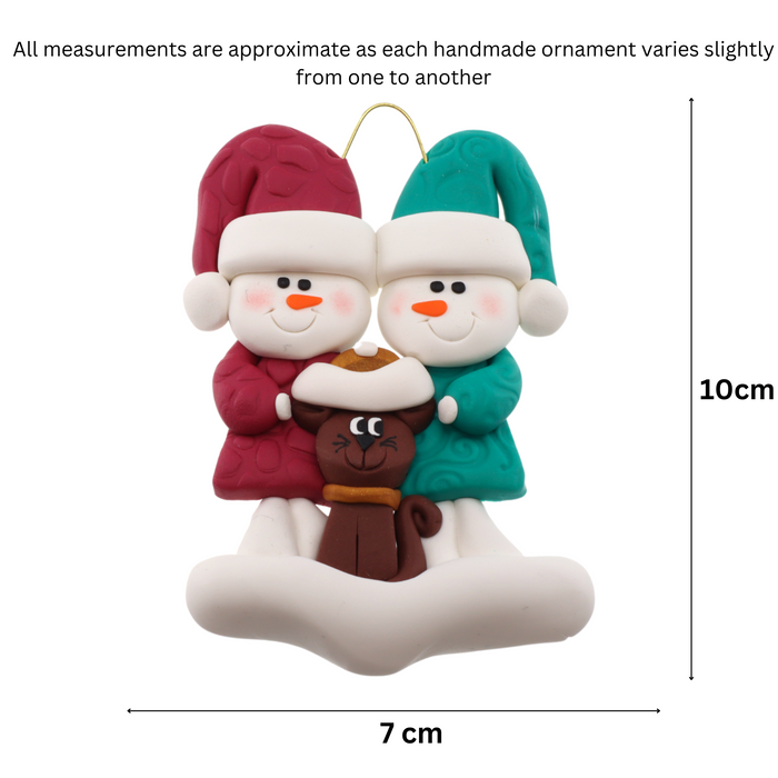 Ornament of snowman couple in red and green shirts and hats with a brown cat in Christmas hat, graphed to show size (7x10cm).