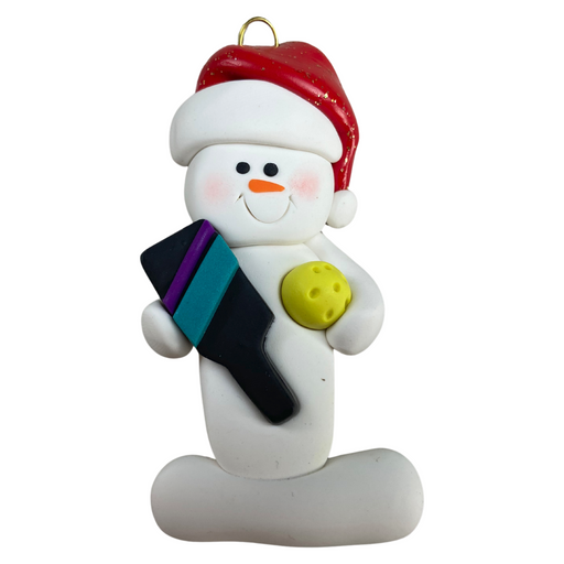 Ornament of white snowman in red hat holding a pickleball paddle and yellow pickleball.