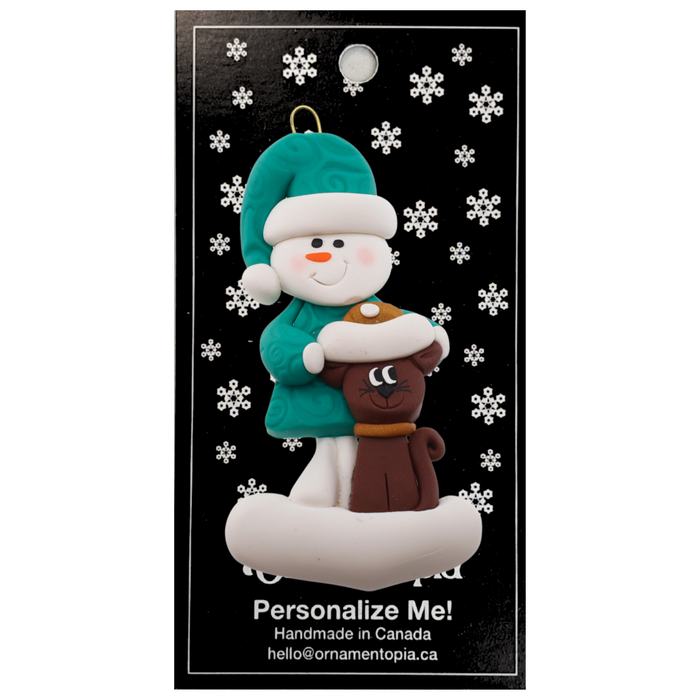 Ornament of snowman in a green shirt and hat with brown cat in Christmas hat, on display backing card.